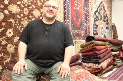 Gencer Gokeri, the owner of Fremont's Istanbul Imports, sits on a stack of handmade, tribal rugs that he brought over from Turkey. (Photo by Allison Int-Hout)