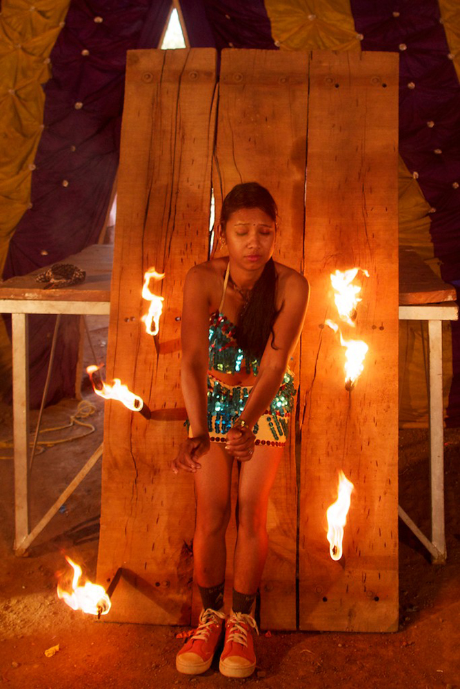 A girl reacts as a blindfolded man throws burning knives towards her.