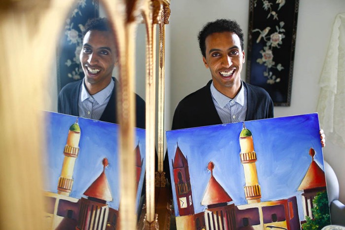 Abraham Tesfasilasie, 21, holds his oil painting entitled, "United", at his apartment in Seattle. Tesfasilasie, along with a friend and fellow artist, is putting on an art show on July 10th to help raise money to perform dental work he needs. The art piece depicts a scene from Asmara, the capitol of Eritrea, where he is from. (Photo by John Lok / The Seattle Times) 