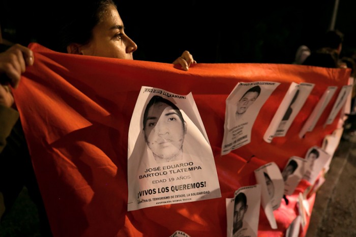 A student at the National Autonomous University of Mexico holds up a banner with the faces of the 43 missing students from Ayotzinapa. (Photo from Flickr by Montecruz Foto)