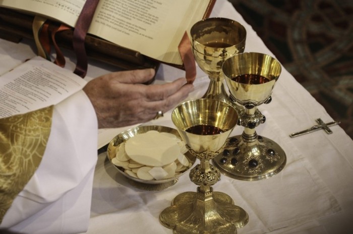 A priest prepares the eucharist for Communion. (Photo by Lawrence OP via Flickr.)