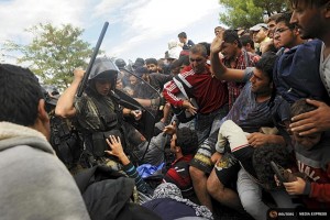 A police officer beats back migrants trying to enter into Macedonia from Greece. (Photo from REUTERS/Alexandros Avramidis)