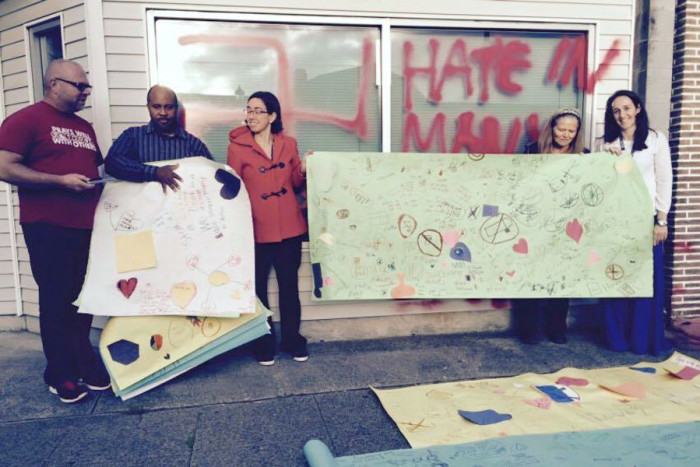 Amor Spiritual Center's Rev. Allen Mosely (left) stands next to his husband Tony Winsely, who is also the choir director, as teachers offer posters with messages of love made by students at Beacon Hill International School. (Photo by Emma Moreno.) 