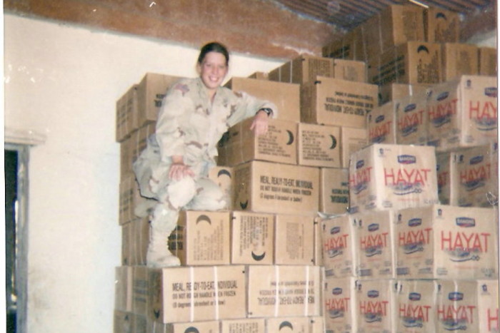 Stephanie Morgareidge sits on boxes of Meals Ready to Eat (MRE) and water supplies in Mosul, Iraq in 2003. Her job dealt with supplying , and her first job stateside at Home Depot as a receiving clerk fit into those skills. (Photo provided by Stephanie Morgareidge)