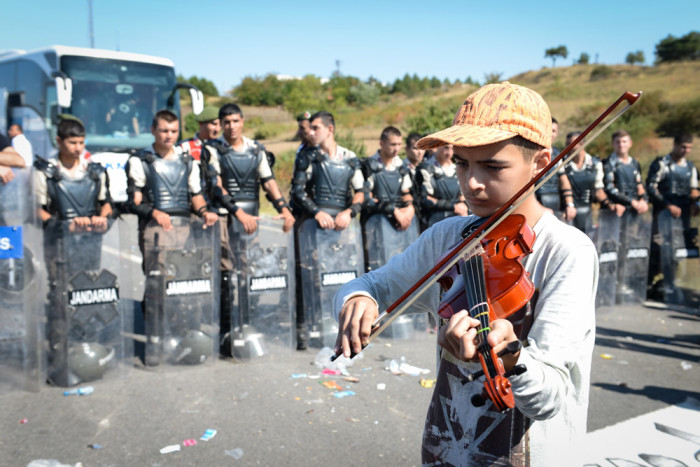 A young refugee plays violin in front of a line of Turkish police at Edirne, where refugees amassed hoping to cross into Greece. (Photo by Levent Kulu)