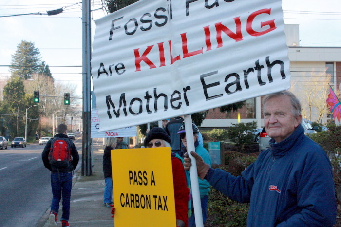 Frank Turner of Olympia holds up a sign in support of Initiative 732, a carbon tax that will go before the state legislature starting in January. (Photo by John Stang)
