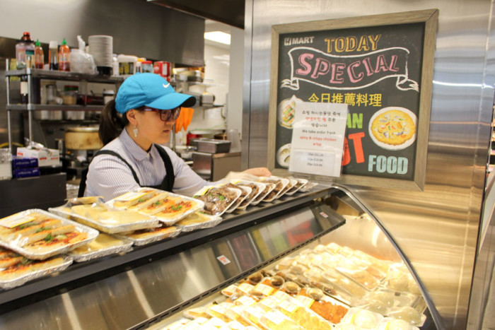 Cashier Susie Hughes arranges the lunchtime deli offerings at the Bellevue H-Mart. (Photo by Venice Buhain.)