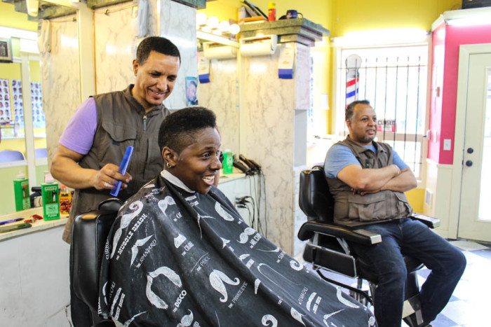 Barber Daniel Abaynhe (right) finishes up Tracey D. Watkin's hair at Update barber shop on 23rd, as barber Adal Shimelis chats with them. (Photo by Venice Buhain.)