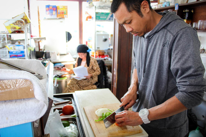 Abodolloh Zay (front) chops vegetables at First Cup Coffee as his mother, coffeeshop owner Nop Zay, does the books. Their business has dropped significantly since the start of road construction on 23rd. (Photo by Venice Buhain.)