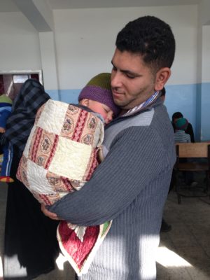A Syrian father and son receive a handmade quilt from Quilts Beyond Borders. The child's mother died in delivery six months earlier while the family awaited entry into Jordan as refugees. (Photo courtesy of Salaam Cultural Museum.)
