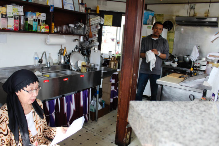 Nop Zay, left, examines paperwork at her coffee kiosk on 23rd Avenue as her son, Abodolloh Zay (right) works in the kitchen. (Photo by Venice Buhain.)