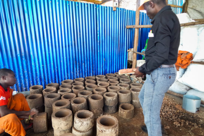 Barnabas Bwambare, standing, a supervisor with Adapt+ Limited, inspects the production of energy-efficient stoves at Kyaka II, a refugee settlement. The stoves are distributed to refugees for free. (Photo by Edna Namara, GPJ Uganda)