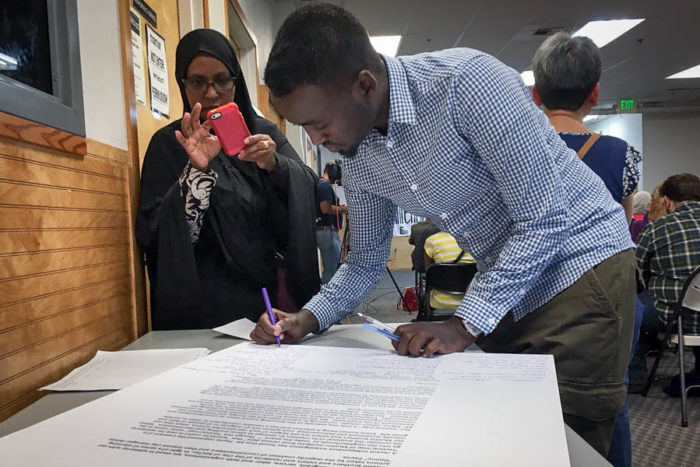 Amina Ahmed, of SeaTac, takes a photograph of Awdoon Mohamed, as he signs a letter to Attorney General Bob Ferguson urging his office to investigate the city of SeaTac. (Photo by Venice Buhain)