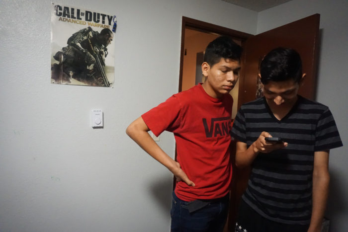 Ricardo, at right, looks at something on his phone while his brother watches alongside him. (Photo by Agatha Pacheco)
